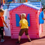 Trzech chłopców stoi na placu zabaw wokół rózowego domku z plastiku