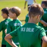 Chłopcy w zielonych koszulkach z białym napisem UKS Orlik stoja na murawie boiska