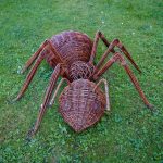 Rrzeźba pająka z ciemnobrązowej wikliny ustawiona na trawniku