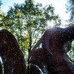 Rrzeźba smoka z ciemnobrązowej wikliny ustawiona na tle drzew